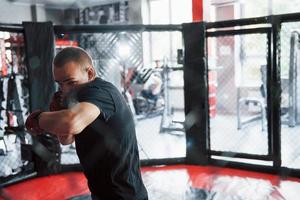 vista frontal. jovem boxeador em bandagens vermelhas tem exercício. no ginásio na jaula foto