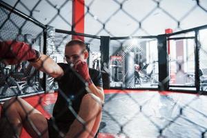 da posição para baixo. jovem boxeador em bandagens vermelhas tem exercício. no ginásio na jaula foto