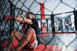 da posição para baixo. jovem boxeador em bandagens vermelhas tem exercício. no ginásio na jaula foto