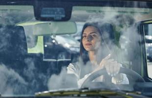 reflexo das nuvens no vidro. vista frontal da mulher que dirige carro novo moderno na cidade foto