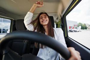 proprietário feliz. vista frontal da mulher que dirige carro novo moderno na cidade foto