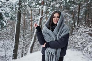 madeiras frias e garota gostosa. retrato de mulher encantadora na jaqueta preta e cachecol cinza na floresta de inverno foto