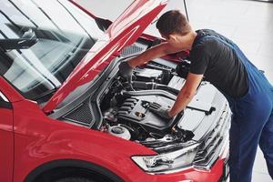 vista superior do trabalhador masculino de uniforme que conserta automóvel vermelho foto