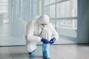 cientista médico masculino em jaleco, óculos de proteção e máscara usando material protetor nas pernas foto