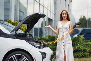 perguntando sobre a nova tecnologia. mulher na estação de carga de carros elétricos durante o dia. veículo novo foto