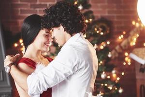 dançando juntos. lindo casal comemorando o ano novo na sala decorada com árvore de natal atrás foto