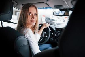 humor alegre. linda loira sentada no carro novo com interior preto moderno foto