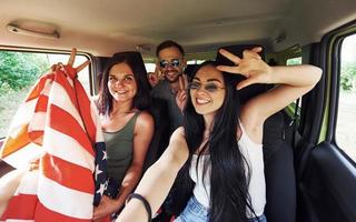 amigos fazendo selfie quando se senta dentro de casa com a bandeira americana nas mãos foto