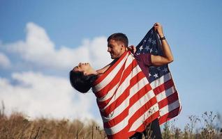 sente liberdade. lindo casal com bandeira americana se diverte ao ar livre no campo foto