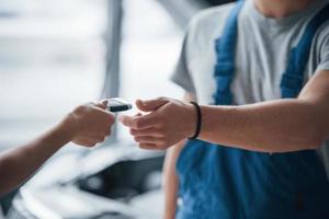 use seu carro completamente reparado com alegria. mulher no salão de beleza com funcionário de uniforme azul levando seu veículo consertado de volta foto