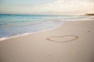 coração desenhado na areia de uma praia tropical foto