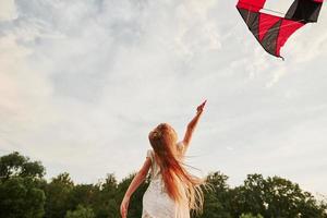 luz do sol quente em uma criança. garota feliz em roupas brancas divirta-se com pipa no campo. natureza bela foto