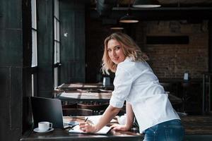 olhando para o lado. mulher de negócios com cabelo loiro encaracolado dentro de casa no café durante o dia foto