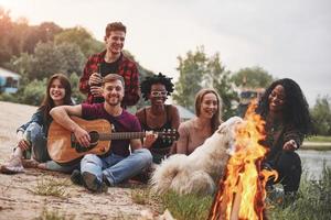 na hora do pôr do sol. grupo de pessoas faz piquenique na praia. amigos se divertem no fim de semana foto