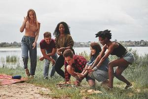 acendendo a fogueira. grupo de pessoas faz piquenique na praia. amigos se divertem no fim de semana foto