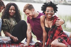 casal internacional. grupo de pessoas faz piquenique na praia. amigos se divertem no fim de semana foto