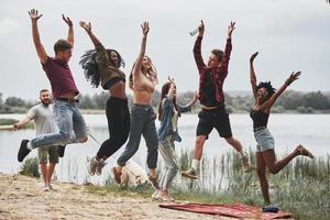 foto no ar. todo mundo está pulando. grupo de pessoas faz piquenique na praia. amigos se divertem no fim de semana