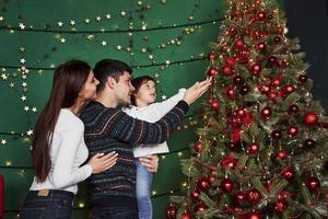 aproveitando as férias juntos. família feliz comemorando o ano novo e em pé perto da árvore de natal foto