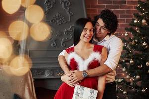 felizes juntos neste dia. lindo casal comemorando o ano novo na sala decorada com árvore de natal e lareira atrás foto