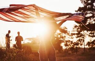 amigos tenham um bom fim de semana ao ar livre perto do carro verde deles com a bandeira dos eua foto