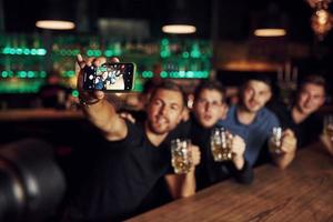 fazendo uma selfie. três amigos descansando no bar com cerveja nas mãos. conversando foto