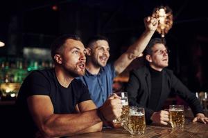 comemorando a vitória. três fãs de esportes em um bar assistindo futebol. com cerveja nas mãos foto