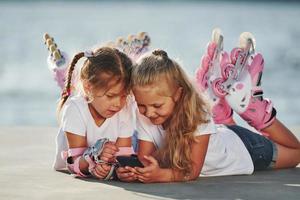 usando smartphones. duas meninas com patins ao ar livre perto do lago ao fundo foto