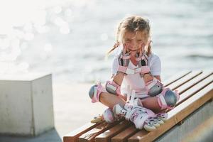 menina bonitinha com patins ao ar livre perto do lago no fundo foto