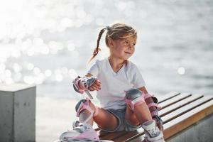 menina bonitinha com patins ao ar livre perto do lago no fundo foto