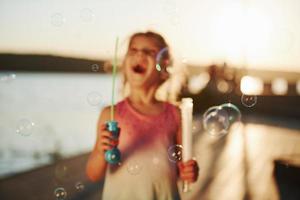 sol incrível. menina feliz brincando com bolhas perto do lago no parque foto