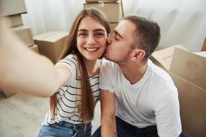 fazendo uma foto. cara beija sua esposa. casal jovem alegre em seu novo apartamento. concepção de movimento foto