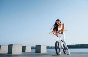 piloto feminino está na bicicleta durante o dia, perto do lago. mulher fitness em roupas esportivas foto