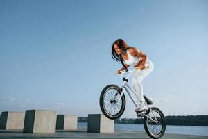 fazendo acrobacias. piloto feminina está na bicicleta durante o dia perto do lago. mulher fitness em roupas esportivas foto