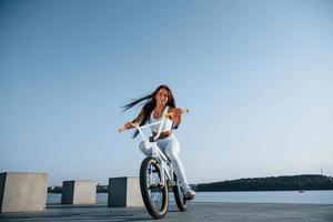 piloto feminino está na bicicleta durante o dia, perto do lago. mulher fitness em roupas esportivas foto