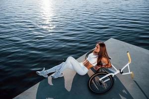 perto da bicicleta. mulher de aptidão descansando perto do lago durante o dia. linda luz do sol foto