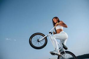 foto em movimento. fazendo acrobacias. piloto feminina está na bicicleta durante o dia perto do lago. mulher fitness em roupas esportivas