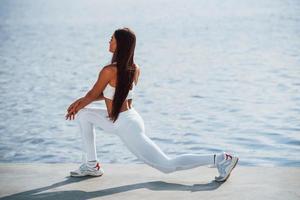 trabalhando nas pernas. tiro de mulher esportiva fazendo exercícios de fitness perto do lago durante o dia foto