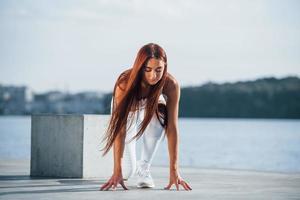 corredor pronto para a ação. tiro de mulher esportiva fazendo exercícios de fitness perto do lago durante o dia foto