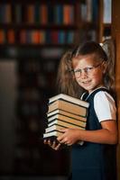 menina bonitinha de óculos fica na biblioteca cheia de livros. concepção de educação foto