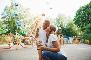 tomando sorvete. menina alegre sua mãe se diverte no parque juntos perto de atrações foto
