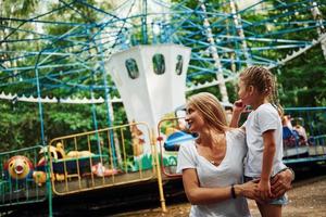 amando um ao outro. menina alegre sua mãe se diverte no parque juntos perto de atrações foto