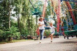 correndo e brincando. menina alegre sua mãe se diverte no parque juntos perto de atrações foto