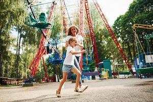 correndo e brincando. menina alegre sua mãe se diverte no parque juntos perto de atrações foto