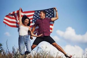 pulando. sente liberdade. lindo casal com bandeira americana se diverte ao ar livre no campo foto