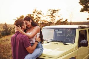 lindo casal beijando ao ar livre. menina senta-se no jipe verde. linda tarde ensolarada foto