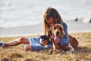 lago atrás. com telefone nas mãos. menina bonitinha passear com seu cachorro ao ar livre em dia ensolarado foto