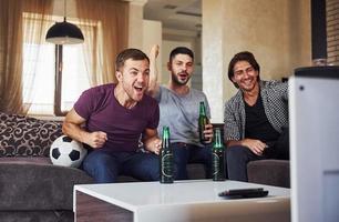 três amigos animados assistindo futebol na tv em casa juntos foto