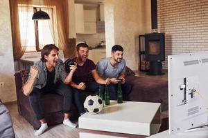 três amigos animados assistindo futebol na tv em casa juntos foto