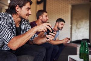 vista lateral. grupo de amigos se diverte jogando jogo de console dentro de casa na sala de estar foto