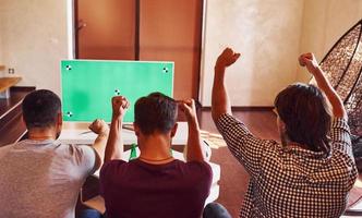 com as mãos para cima. três amigos animados assistindo futebol na tv em casa juntos foto